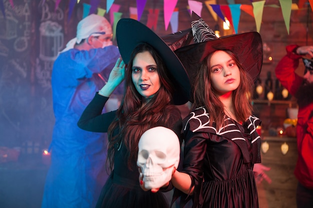 Photo two witches at a halloween celebrating holding a human skull. cheerful witches. looking at the camera.