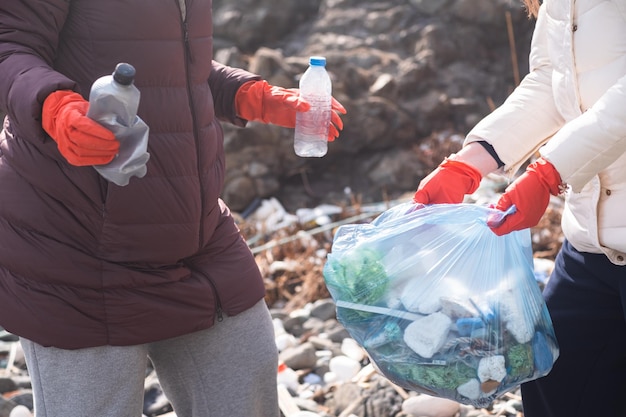 Photo two woman collects plastic garbage in bags on the beach pollution disaster empty plastic bottles