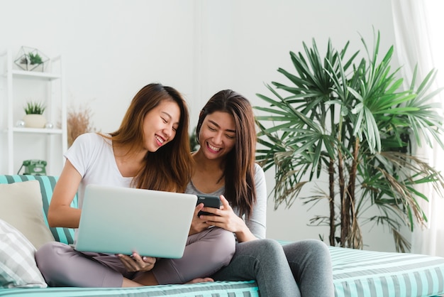 Two woman friends use credit card shopping online with laptop computer sitting on sofa at home