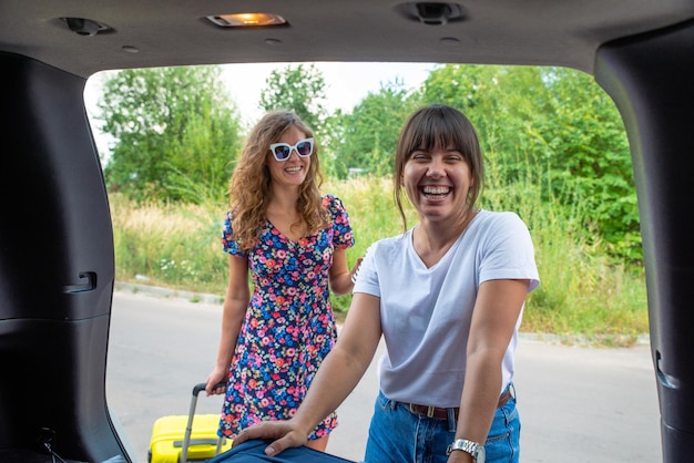 Two woman packing luggage in car trunk