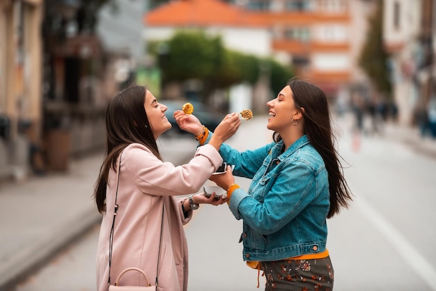 Two woman walking around modern town and eating fresh poffertjes Selective focus