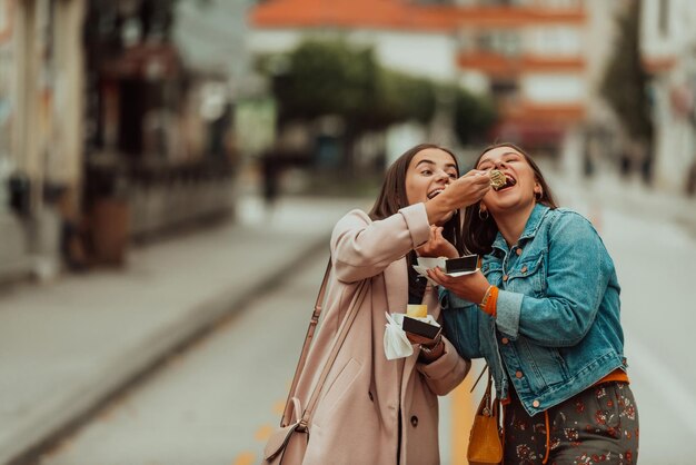 Two woman walking around modern town and eating fresh poffertjes Selective focus