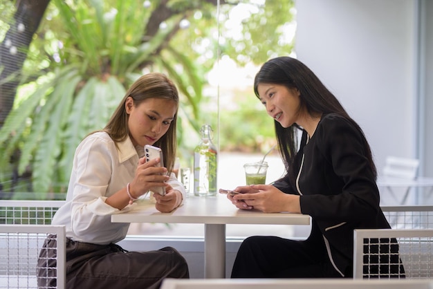 Two women are having a pleasant coffee meeting at a modern cafe with casual and professional vibes while using mobile phone