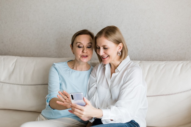 Two women are sitting on the couch and looking at the phone while talking