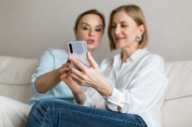 Two women are sitting on the couch and looking at the phone while talking