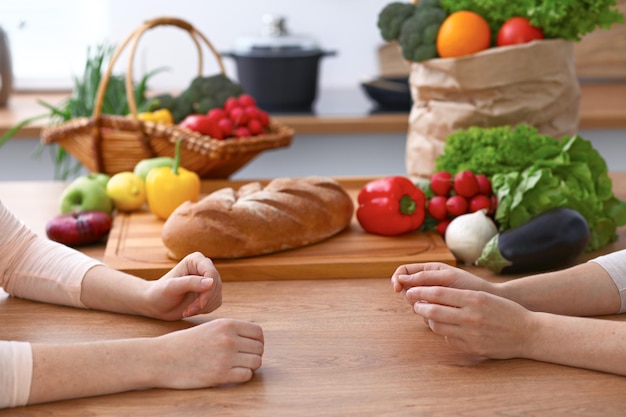 Two women discussing a new menu in the kitchen, close up. Human hands of two persons gesticulating at the table among fresh vegetables. Cooking and friendship concept.