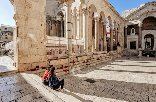 Two women drinking coffee on steps on Peristyle in Diocletian's palace in Split, Croatia.