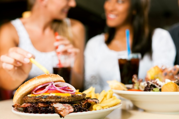 Two women eating hamburger and drinking soda