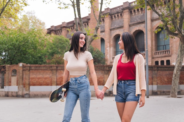 Two women friends walking happy holding hands