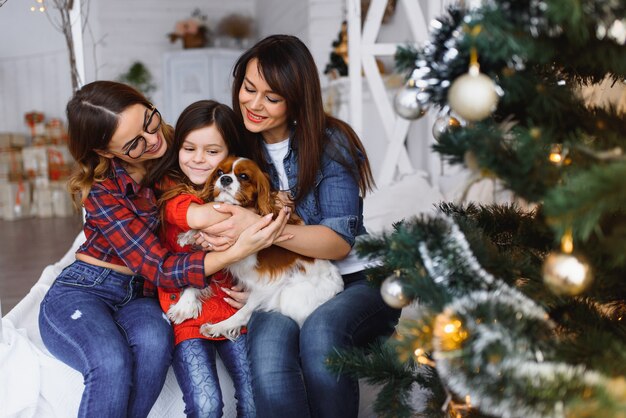 Two women and a girl with a dog have fun near the Christmas tree on Christmas holidays.