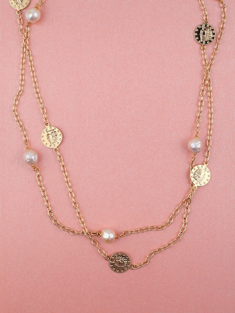 Two women gold necklaces on shimmering pink background Top view