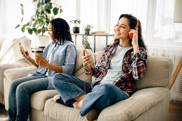 Two women in headphones leisures on sofa