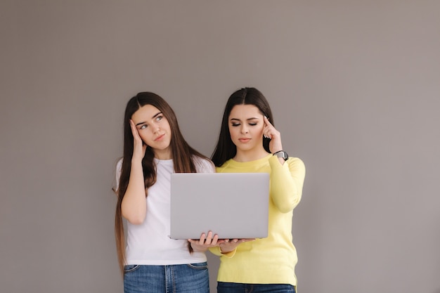 Two women hold one laptop. females think and put finger on temple