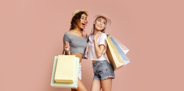 Two Women Holding Shopping Bags Against Pink Background