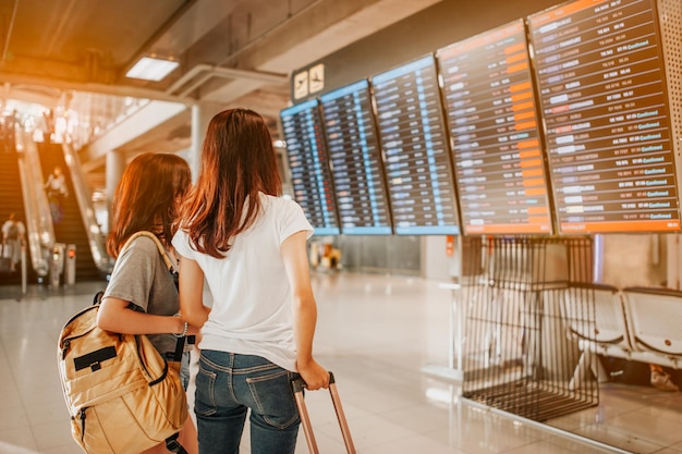 Two women in international airport terminal, looking at information board, checking her flight.