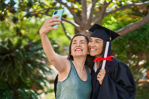 Two women mother and graduated daughter make selfie by smartphone at park