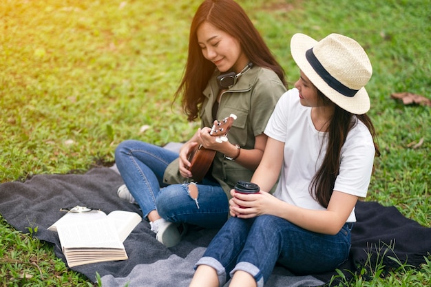 Two women playing ukulele while sitting together in the woods