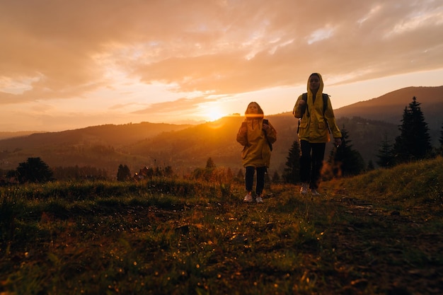 Two women in raincoats on a hike climb a mountain in rainy weather with backpacks on their backs