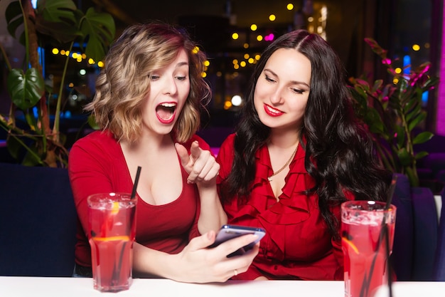 Two women in red dresses drink cocktails and celebrate in a nightclub or bar