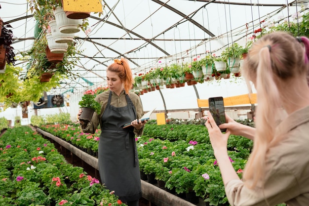 Two women shooting video and photo content for social media of their small business in greenhouse