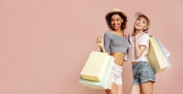 Two Women Shopping With Colorful Bags Against a Pink Background