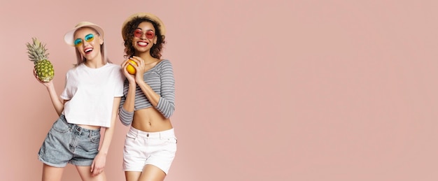 Two Women Smiling And Holding Fruit In Front Of Pink