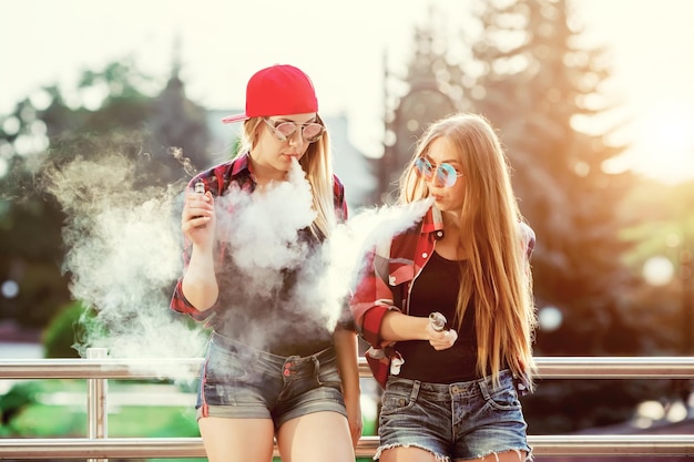 Two women vaping outdoor the evening sunset over the city toned image