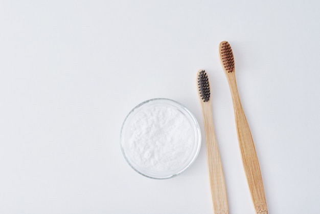 Two wooden bamboo toothbrushes and baking soda powder in glass jar on a pink background.  Teeth health and keep mouth concept