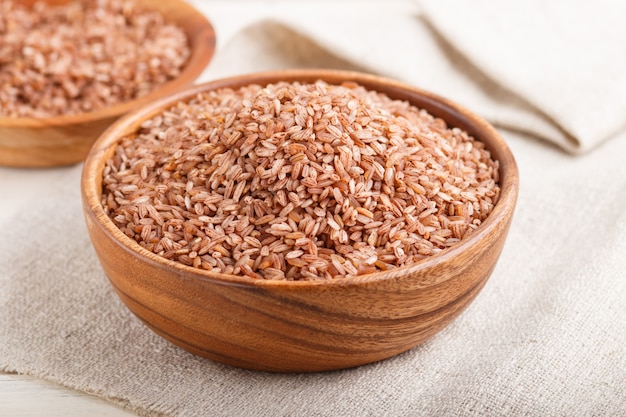 Two wooden bowls with unpolished brown rice. Side view, close up.