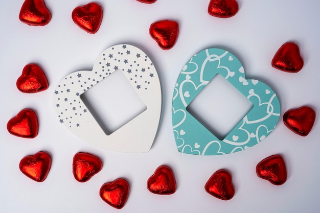 Two wooden colored empty heart-shaped photo frames and lots of shiny heart-shaped candies