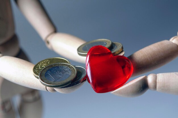 Photo two wooden figures giving each other a red heart and a euro coin