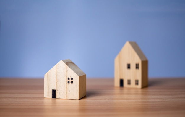 Two wooden model houses placed on a wooden table. with a light blue background