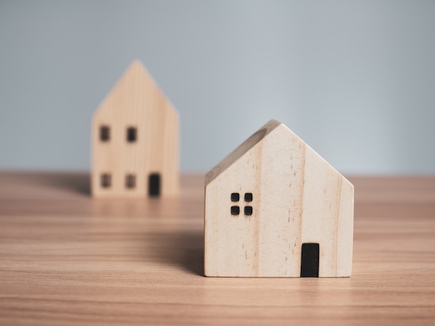 Two wooden model houses placed on a wooden table. with a light gray background