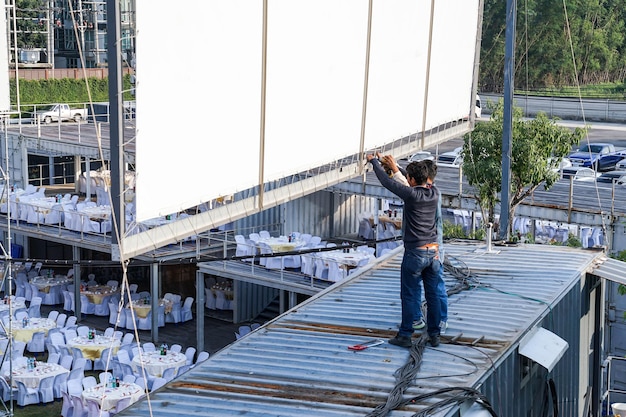 Two worker setup outdoor canvas billboard on the rooftop of container