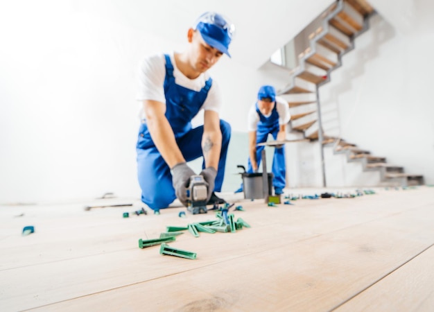 Two workers in a special uniform laying tiles with tile leveling system and laser level on the floor