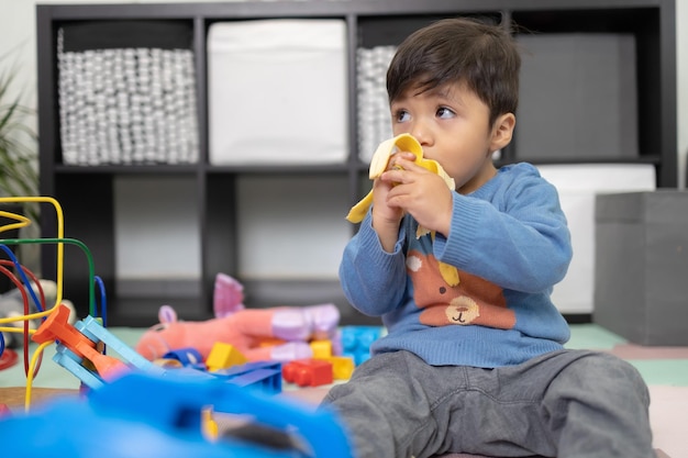 Two years old mexican baby boy eating banana on messy room