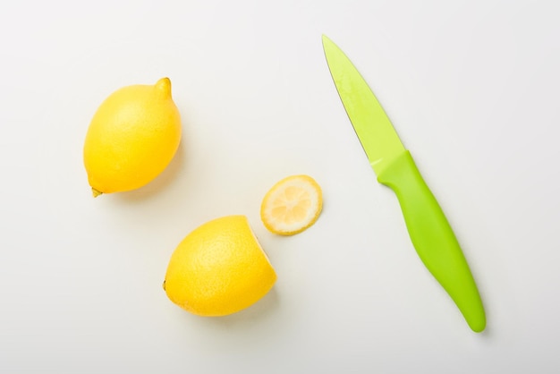 Two yellow citrus lemons with green fruit knife on the white table prepared to cook lemonade