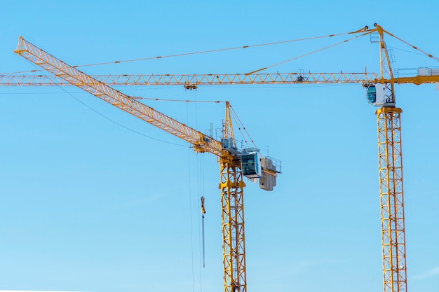 Two yellow construction cranes on blue sky background