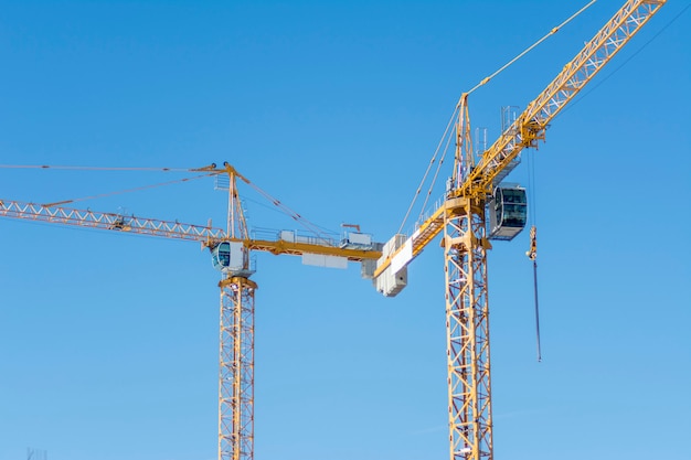 Two yellow construction cranes on blue sky background