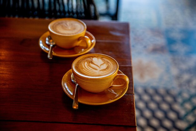 Two yellow cups of hot cappuccino on wooden table background amazin art latte on coffee