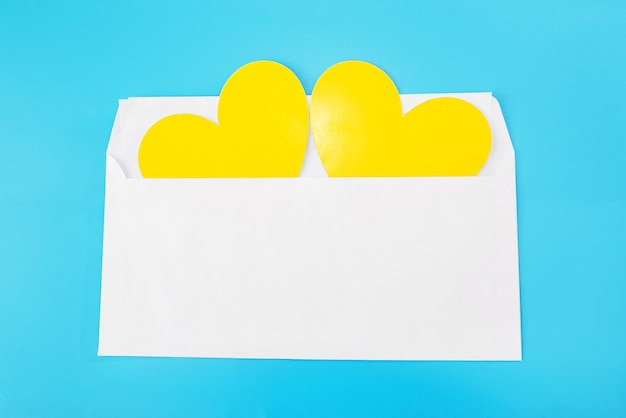 Two yellow hearts in a white envelope isolated on a blue background. Close-up.