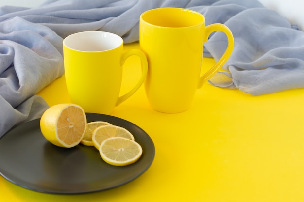 Photo two yellow mugs and sliced lemon on black plate with copy space. trendy colors of the year 2021. illuminating yellow and ultimate grey.