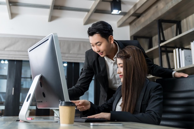 Two young Asian business people meeting and discussing business looking at computer on table working together