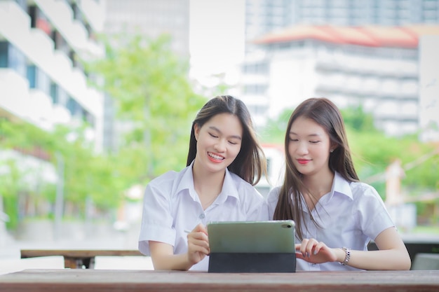 Two young Asian girls students are consulting together and using a tablet to search information