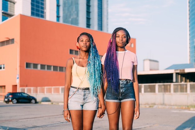 Two young beautiful black sisters holding hands listening music posing