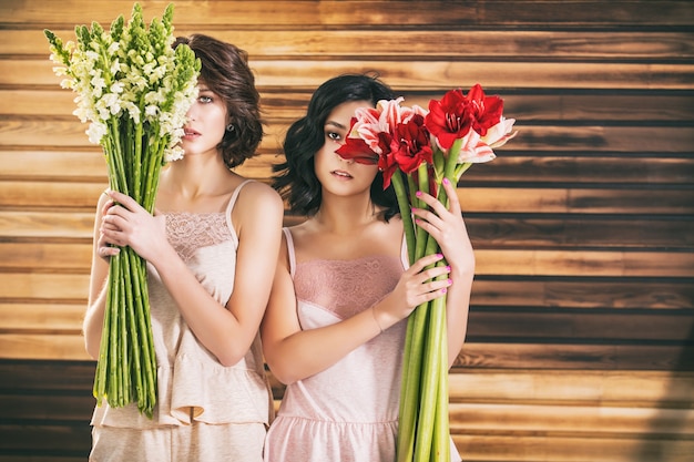 Two young beautiful girl models in delicate lingerie with flowers on wooden background