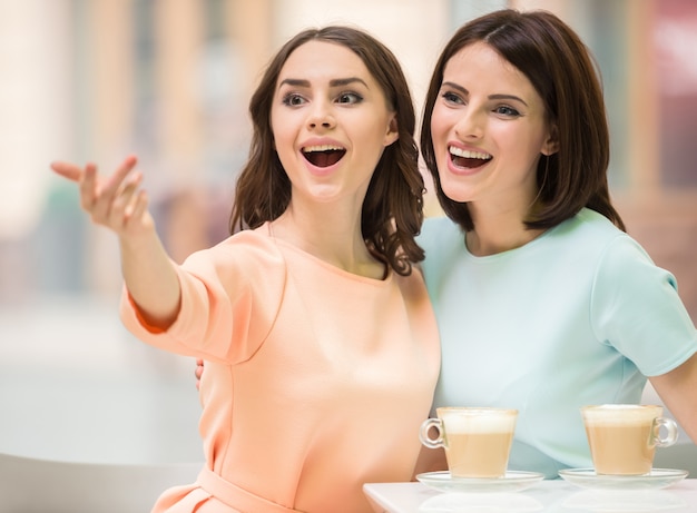 Two young beautiful girls sitting in urban cafe with coffee.