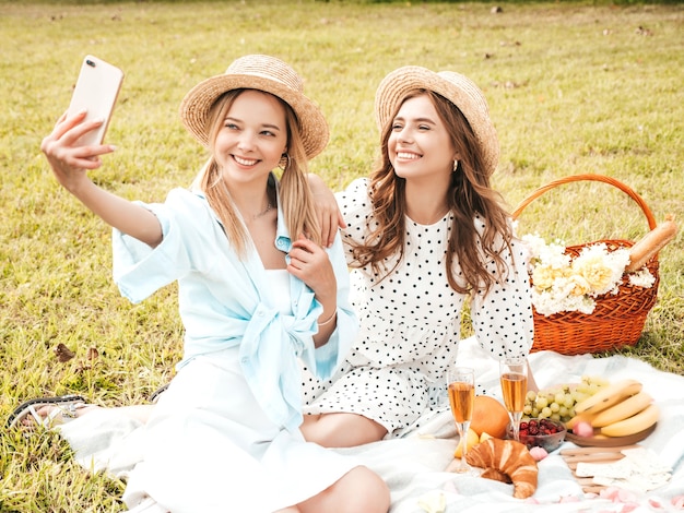 Two young beautiful hipster woman in trendy summer sundress and hats. Carefree women making picnic outside. 