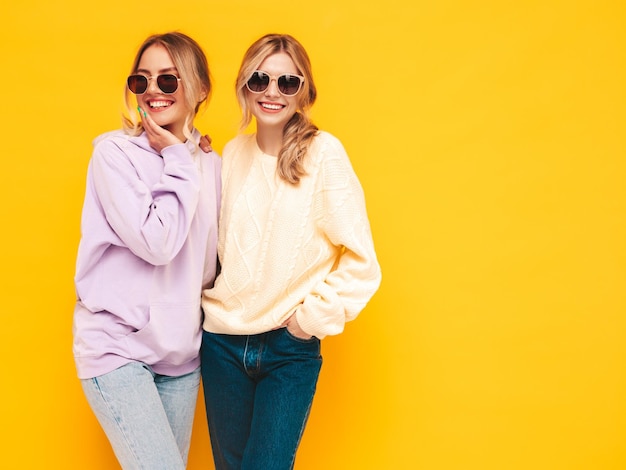 Two young beautiful smiling brunette hipster female in trendy summer clothes Sexy carefree women posing near yellow wall in studio Positive models having fun Cheerful and happy in sunglasses