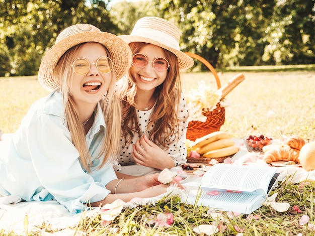 Two young beautiful smiling female in trendy summer sundress and hats.Carefree women making picnic outside.